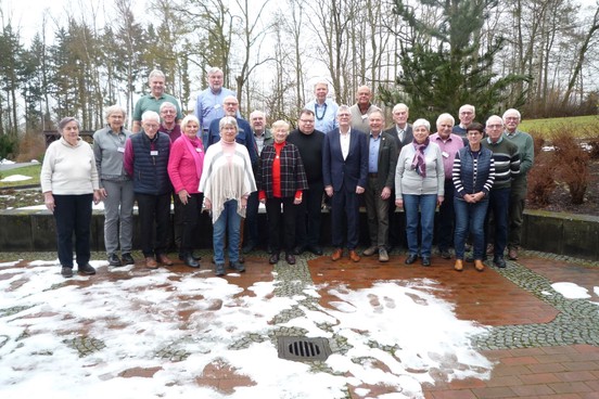 Ein Referent steht in einem Raum vor einer Leinwand. Vor ihm sitzen Zuhörer auf Stühlen.